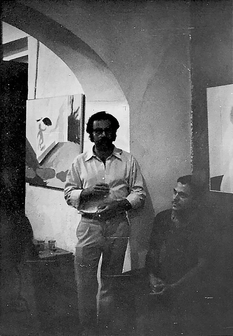 Galeria Ivan Spence, Eivissa, 1967. Dret sota un arc emblanquinat, davant d'una pintura de formes clares; Francesc Parcerisas assegut a l'ombra. Fotografia en blanc i negre, de gra gruixut.