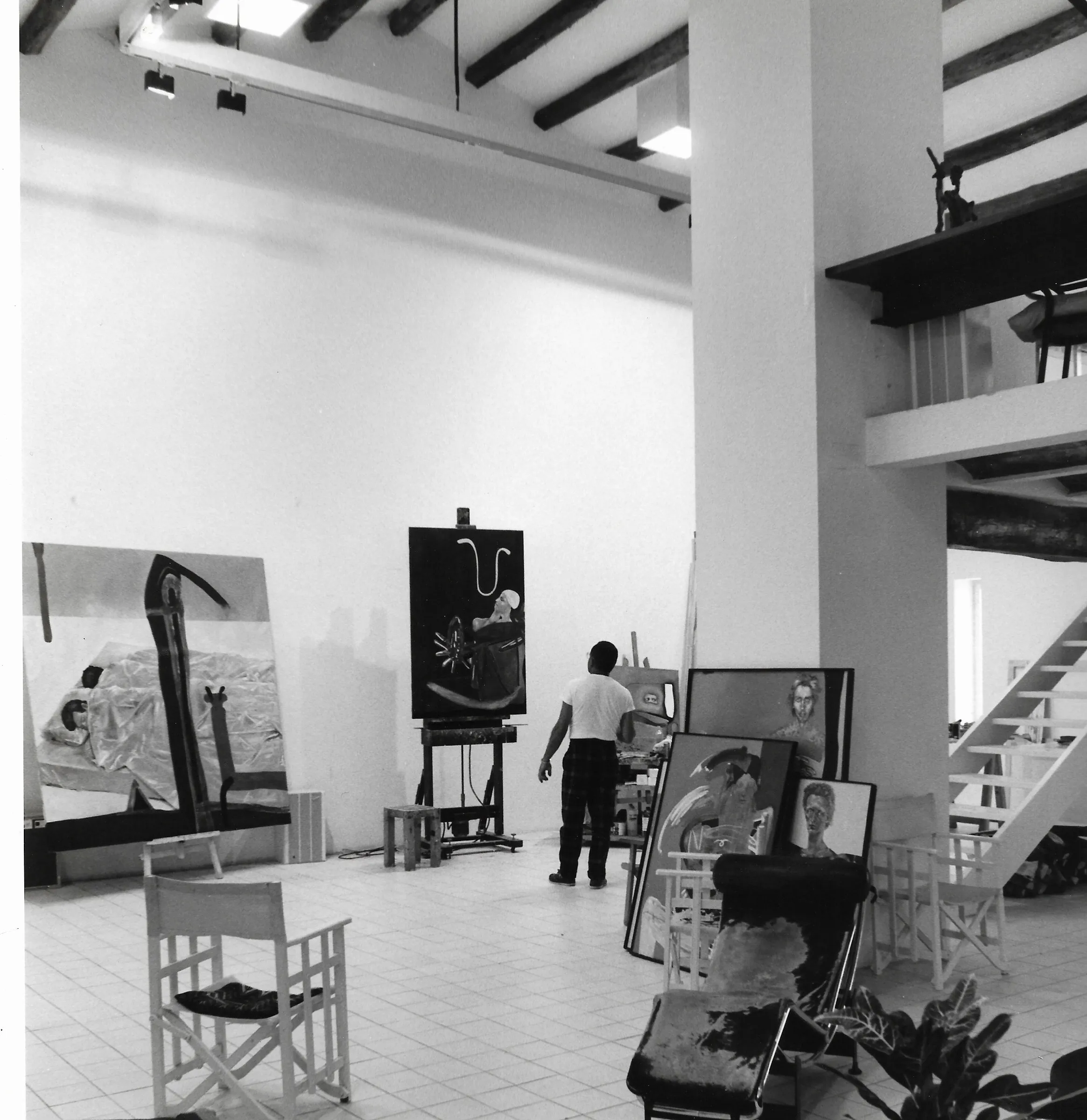 L'estudi de Cadaqués, 1986: sala alta de bigues de fusta, reformada per Lanfranco Bombelli. D'esquena, davant del cavallet; a l'esquerra, una obra gran amb una àncora; retrats emmarcats a terra. Fotografia en blanc i negre.